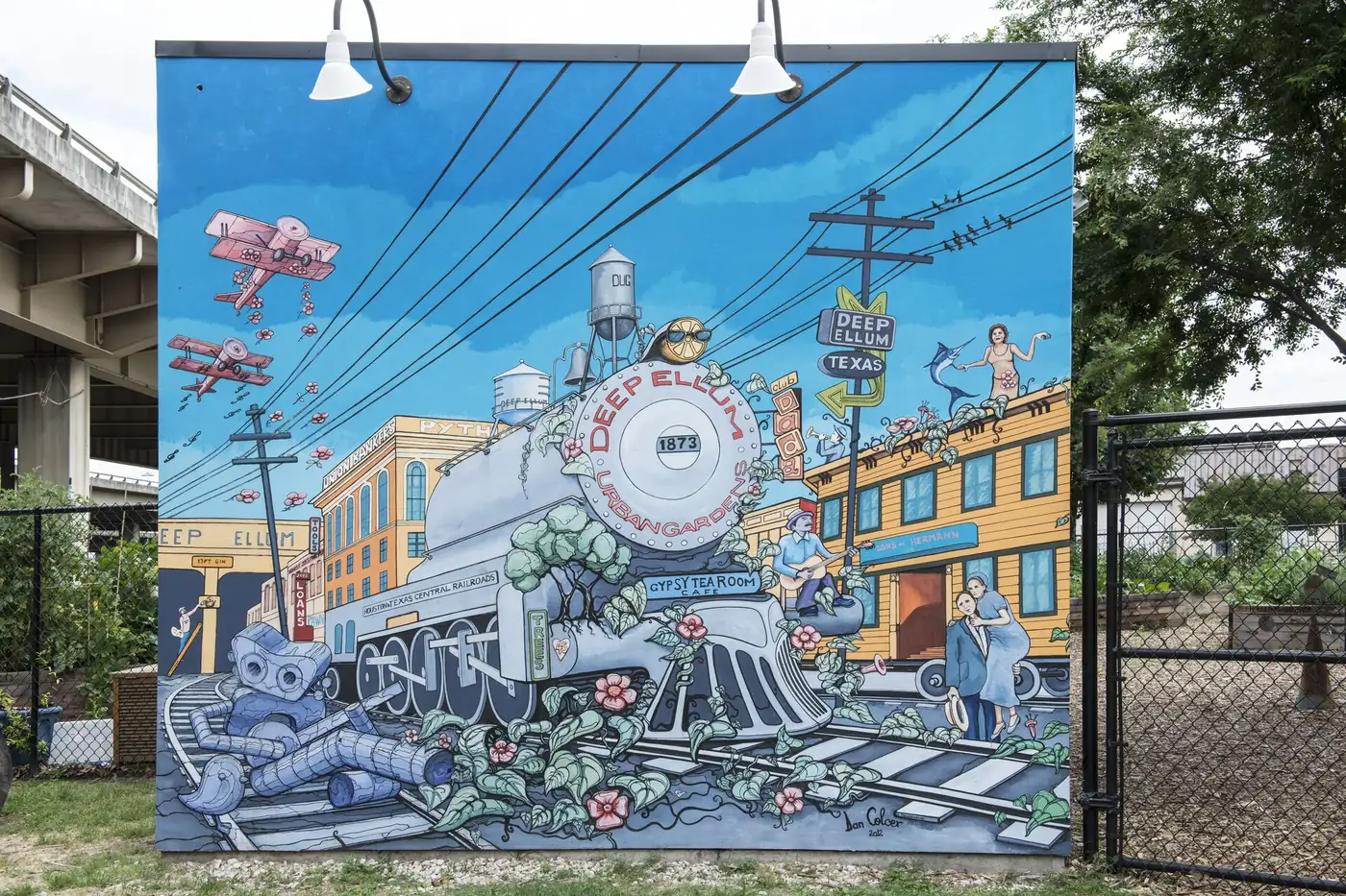 A mural of a steam locomotive and a yellow storefront at the Deep Ellum Urban Garden in Dallas